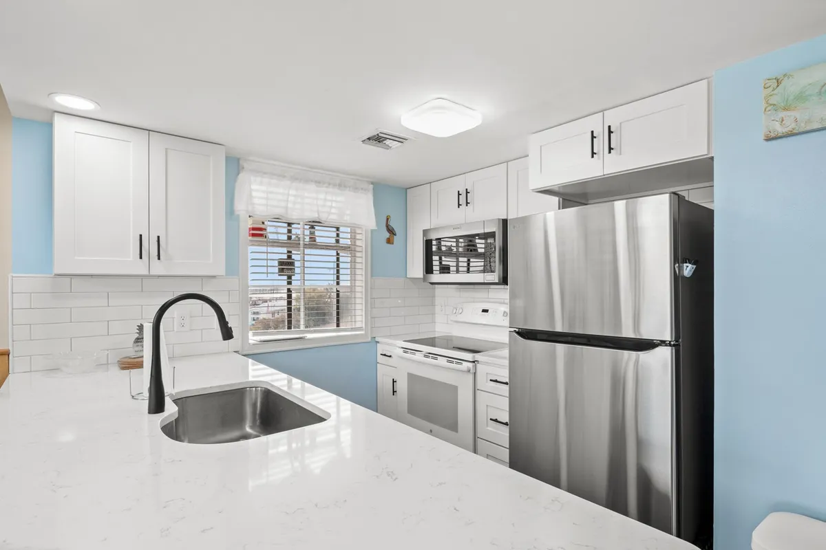 A cheerful kitchen scene highlighting sleek modern appliances, white cabinetry, light blue walls, and polished marble countertops. The arrangement suggests a functional and pleasant space for preparing meals and enjoying everyday routines.