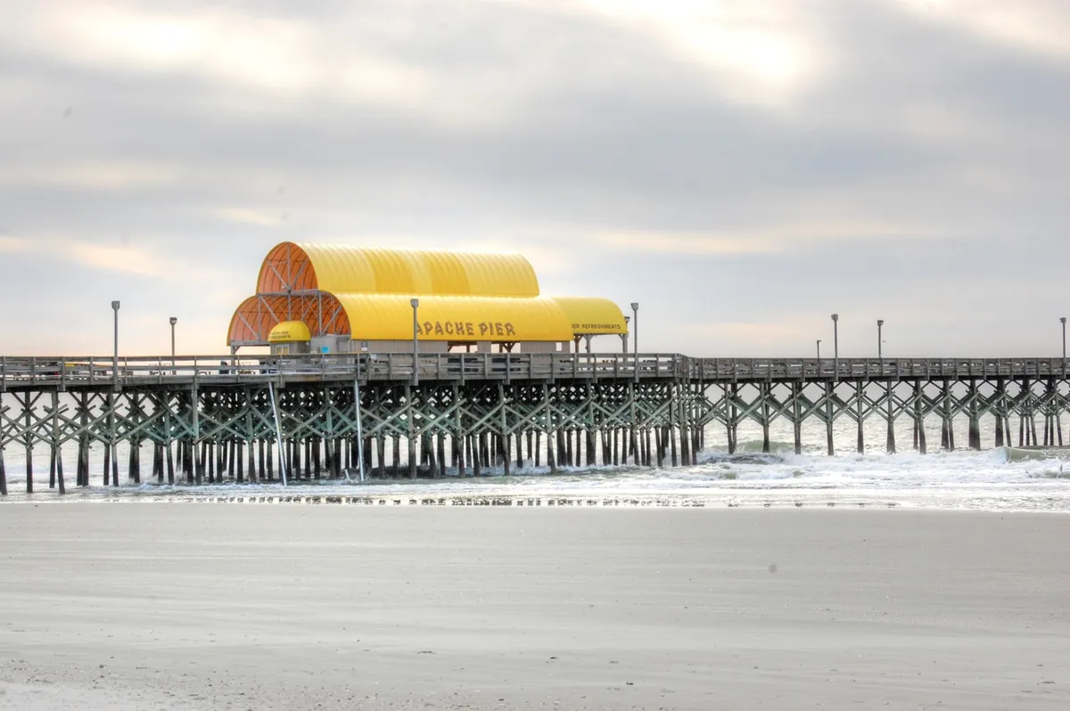 This image showcases the iconic Apache Pier stretching out over the ocean, with gentle waves and a distinct yellow structure visible. The pier is a focal point for fishing, oceanfront walks, and family activities, capturing the essence of one of Myrtle Beach’s beloved attractions.