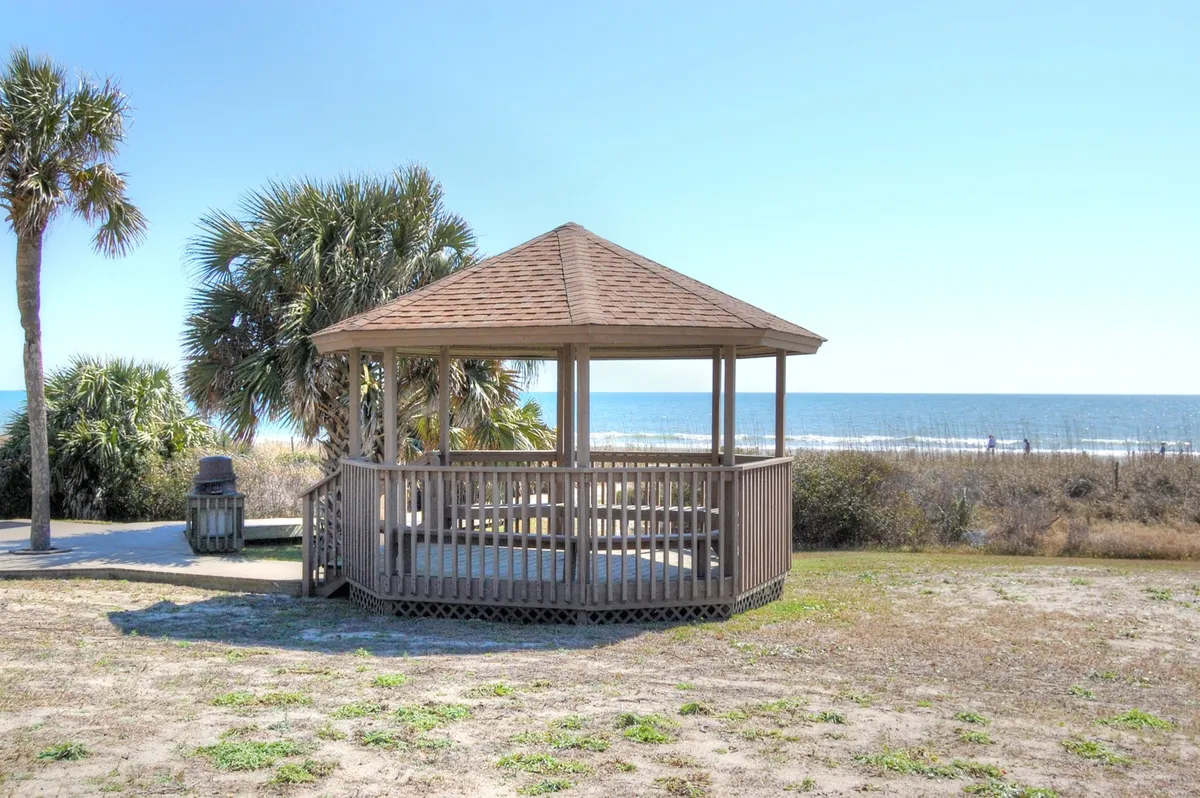 This image captures a serene gazebo nestled among palm trees with a sweeping ocean view in the background. The scene invites relaxation and offers a tranquil spot for couples to unwind, enjoy each other's company, or watch the sunset together.