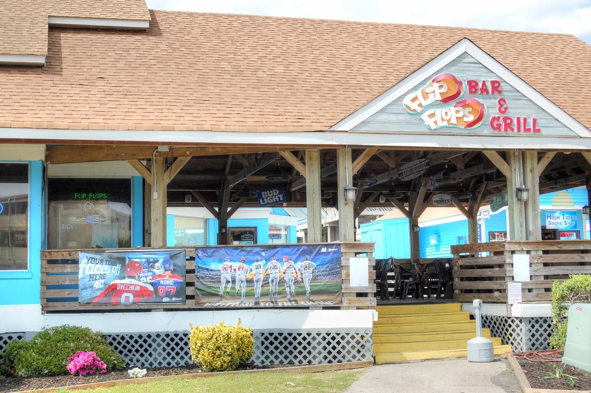 An inviting exterior shot of Flip Flops Bar & Grill, with colorful banners and an outdoor seating area. The scene hints at lively evenings, casual dining, and the chance for couples to enjoy local cuisine together.