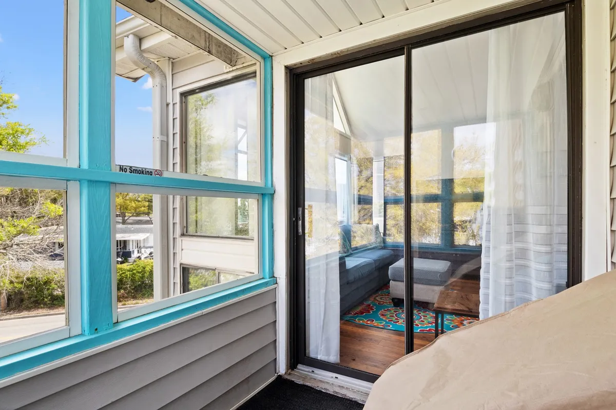 A cozy seating arrangement with turquoise window frames, a colorful area rug, and comfortable chairs. Large windows allow morning light to fill the space, enhancing a welcoming, relaxing vibe that invites conversation or quiet moments.