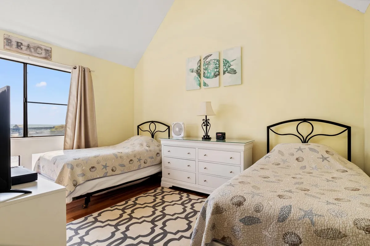 A welcoming bedroom with two twin beds, decorative wall art, dressers, and a television. The room is filled with natural light, creating an inviting space ideal for children or friends to unwind together.